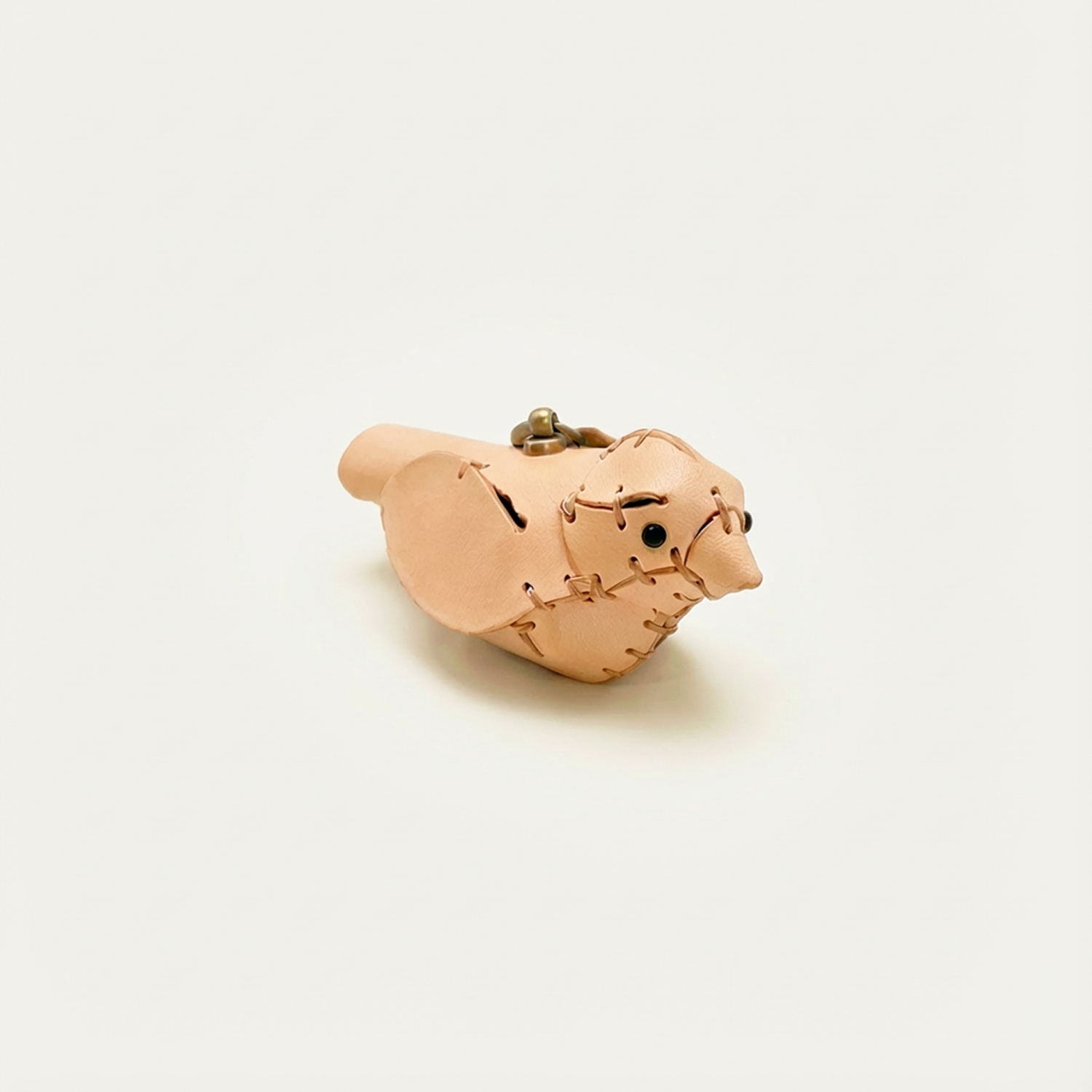 A hand-stitched natural leather little bird with a brass clasp, on an off-white background.