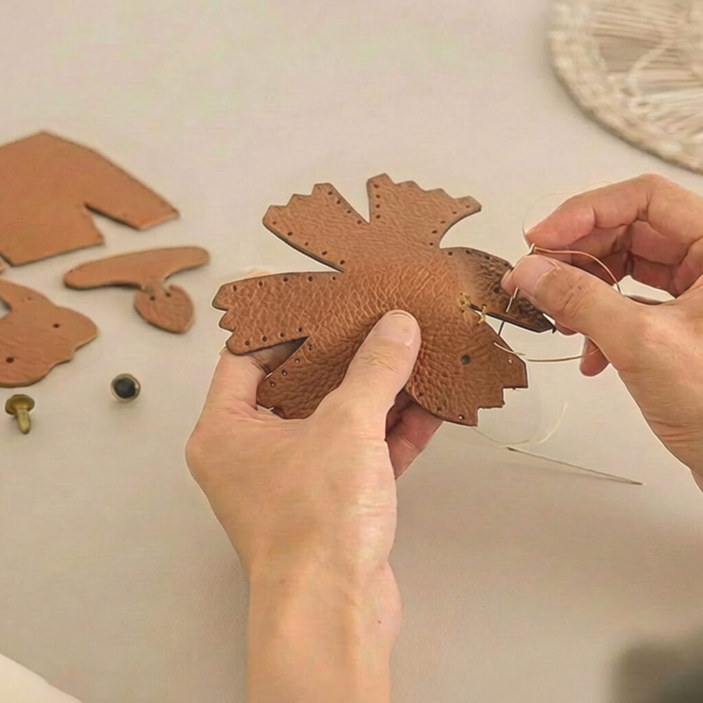Hands stitching pieces of brown leather for a Leather DIY Kit on a quiet worktable.