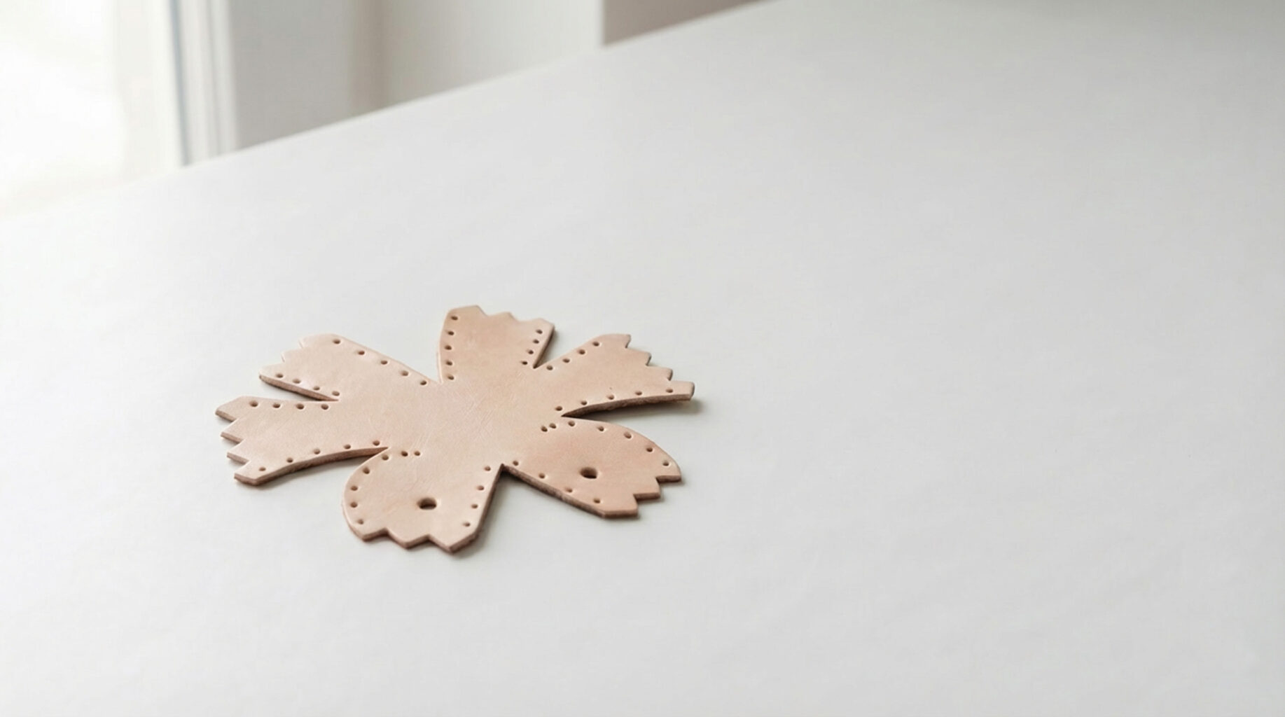 A flat leather DIY kit piece resting on a white table in soft morning light, before stitching begins.
