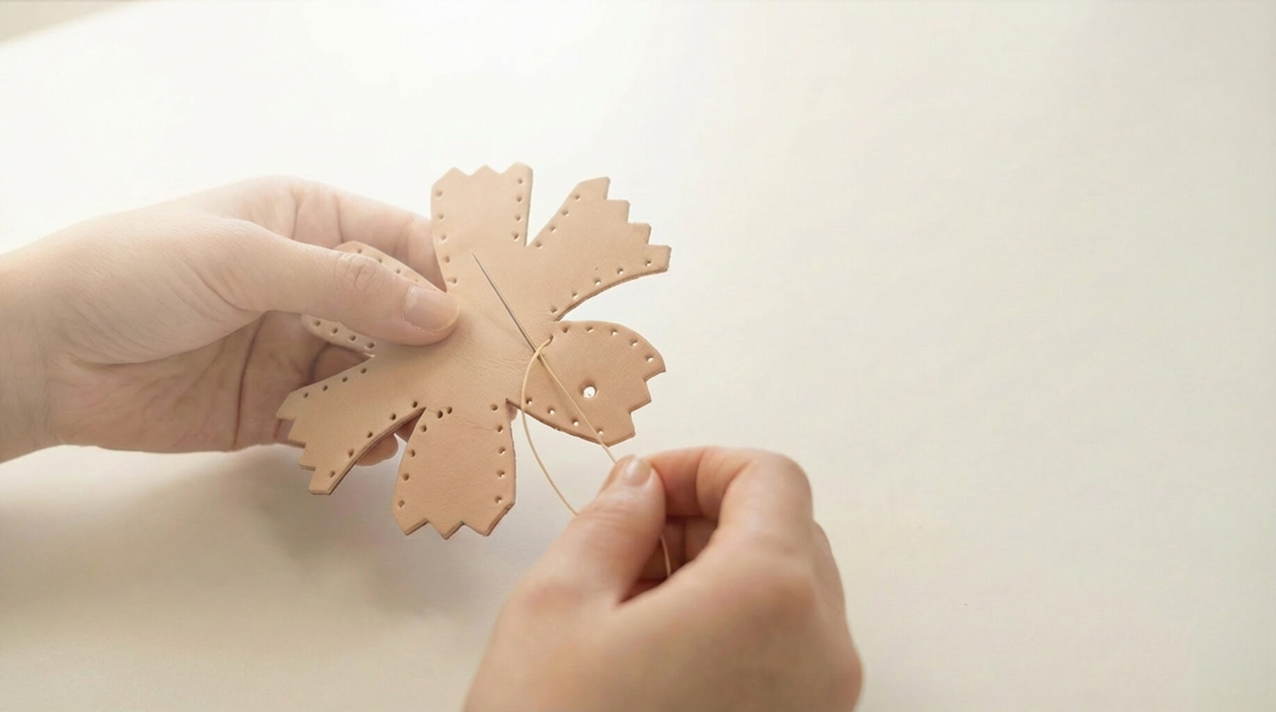 A leather DIY kit part held gently as a needle passes thread through a pre-punched hole, marking the quiet beginning of hand-stitching.