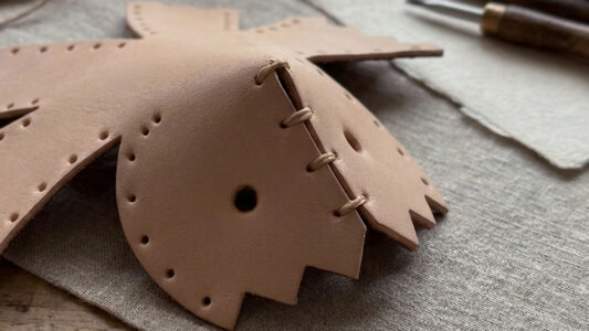 Hand-stitched leather parts beginning to rise from a flat surface, forming the first curve of a leather model.