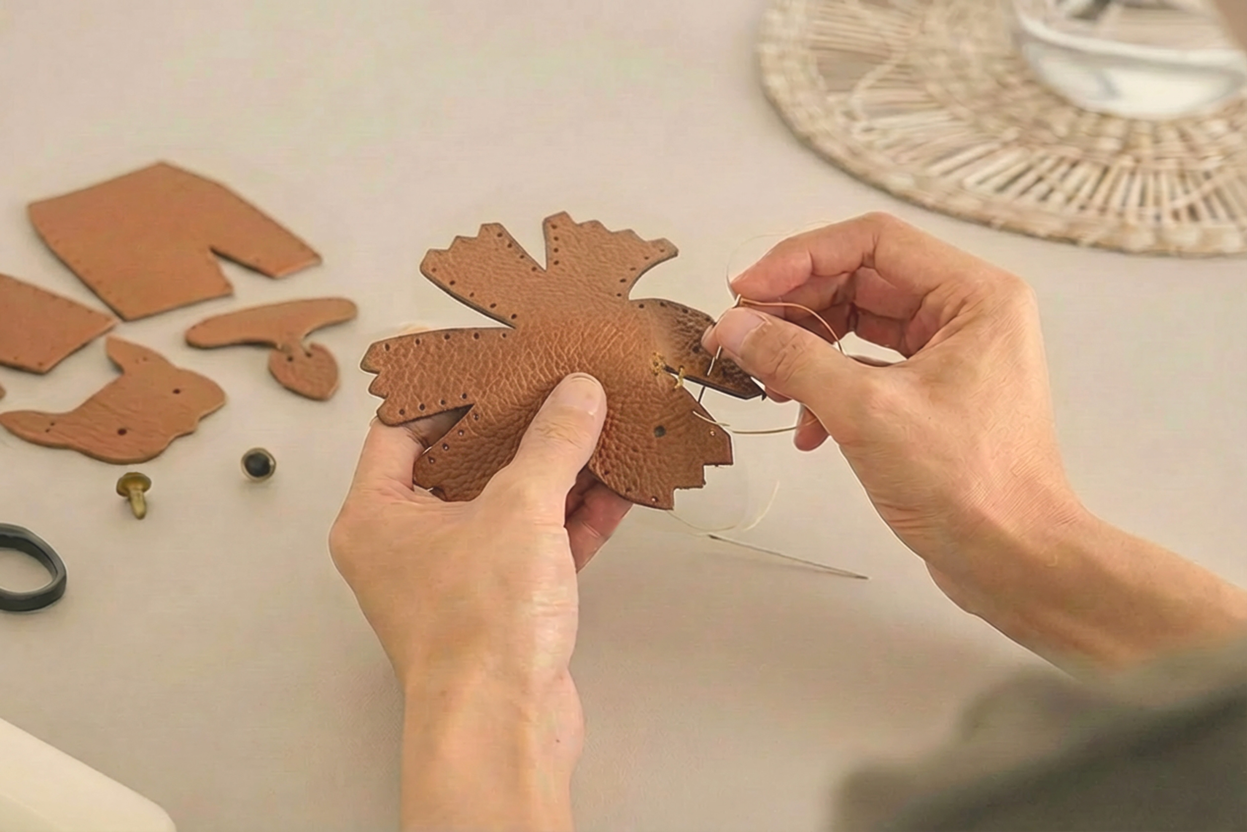 Hands stitching pre-cut leather parts together with waxed thread on a worktable