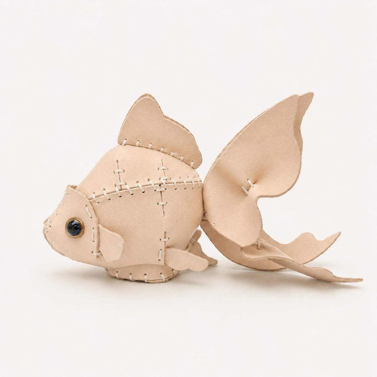 The Natural colourway — a goldfish model in pale veg-tanned leather, hand-stitched, with fanned fins and a gold-ringed eye.