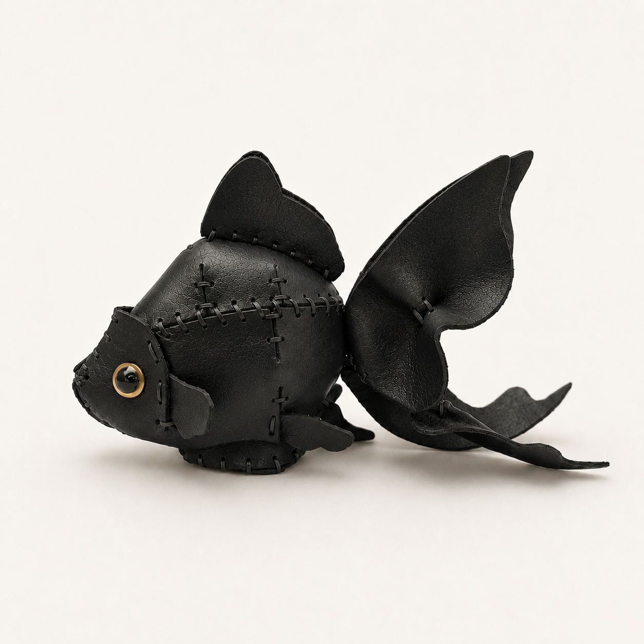 The Black colourway — a goldfish model in black leather, hand-stitched, with fanned fins and a gold-ringed eye.