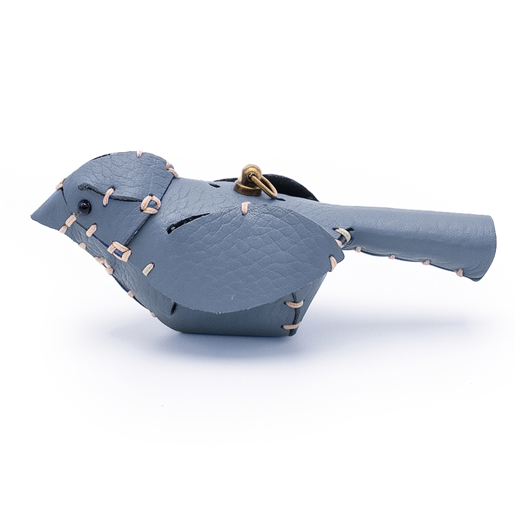 A hand-stitched blue leather little bird with a brass clasp, on an off-white background.