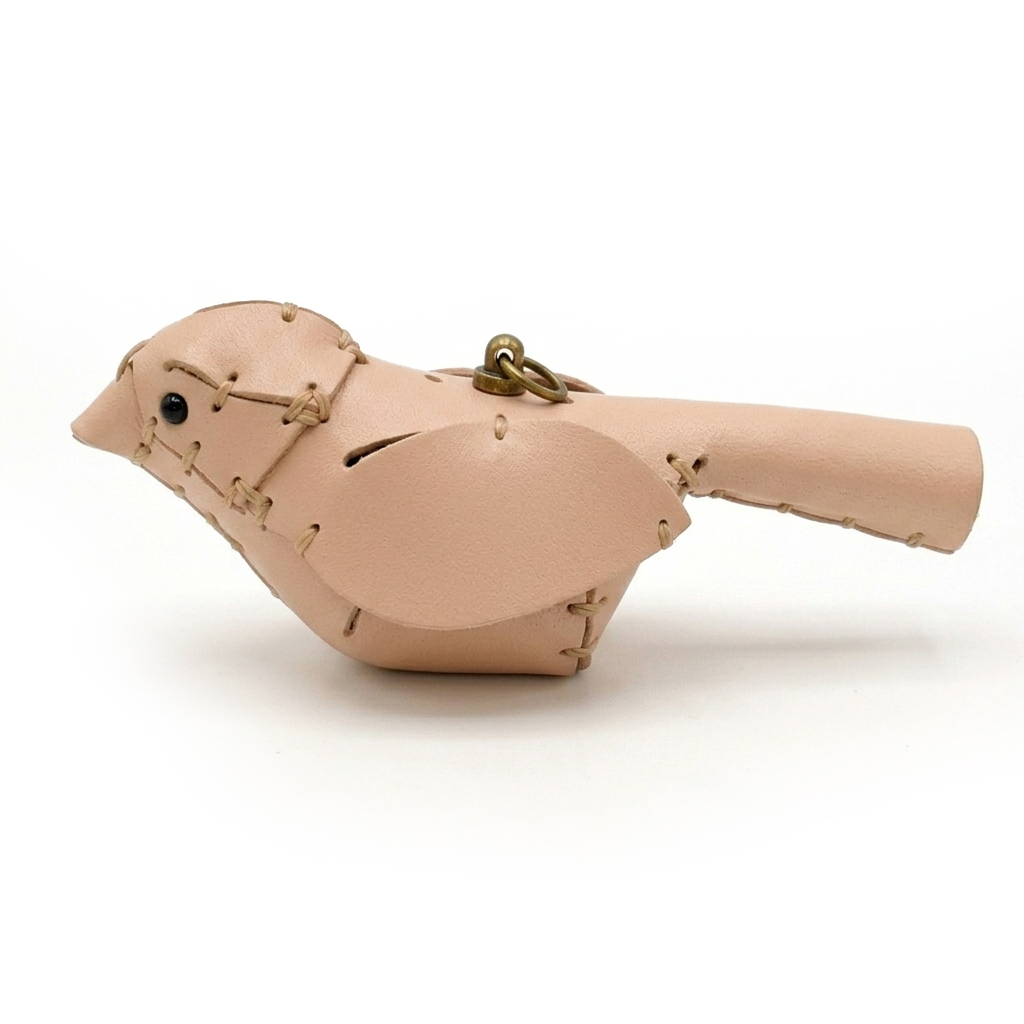 The Natural colourway — a single leather bird in smooth veg-tanned leather, side view, whip-stitched with a black bead eye.